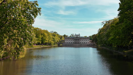 a picturesque shot of pałac na wyspie in warsaw, highlighting the serene lake and greenery