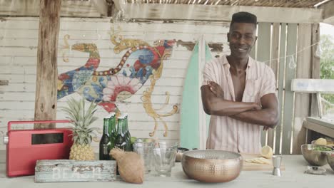 Portrait-of-happy-african-american-barman-standing-behind-the-counter-at-a-beach-bar,-slow-motion