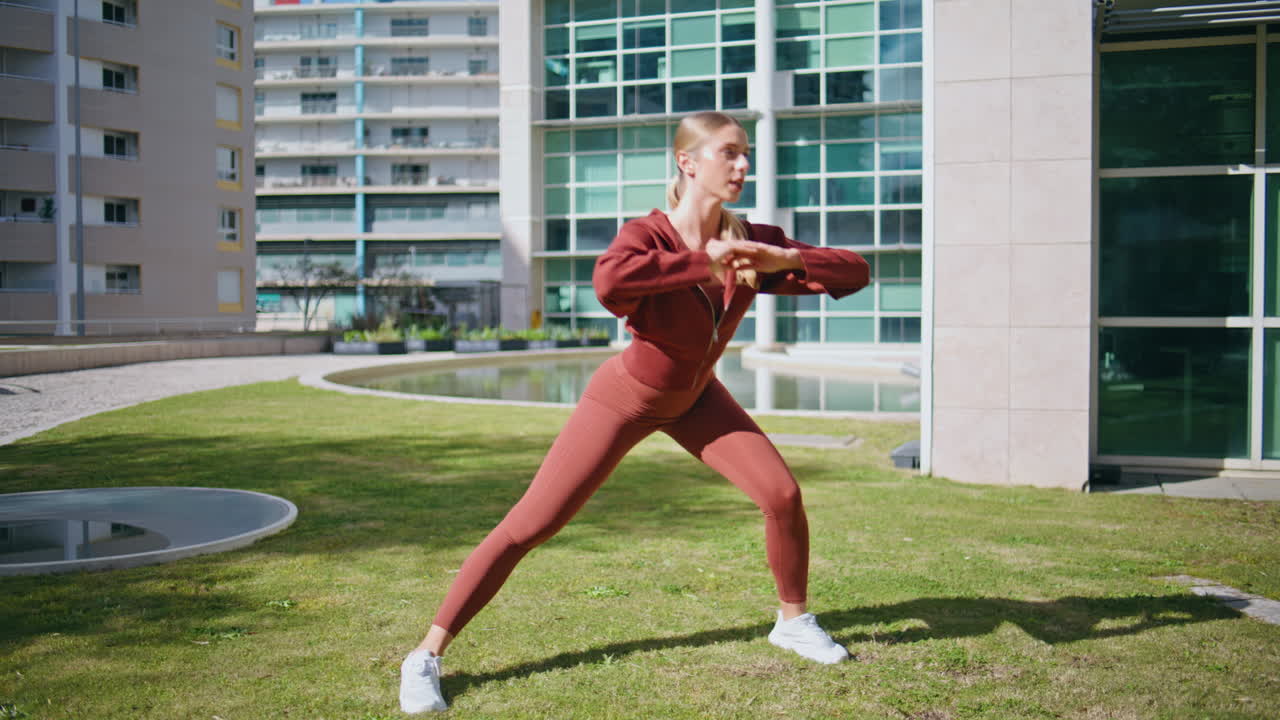 Woman doing sport exercise in sunlight. Urban sportswoman train on green grass