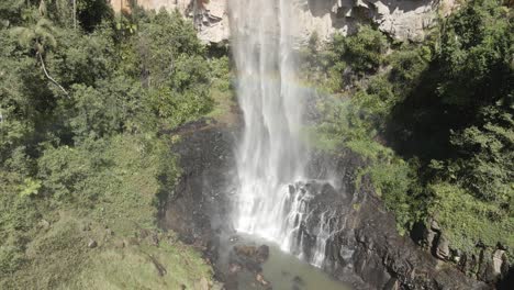 this huge jungle waterfall crashes through lush greenery, mist creating a bright rainbow over the dense landscape. an awe-inspiring display of raw power and tropical beauty.
