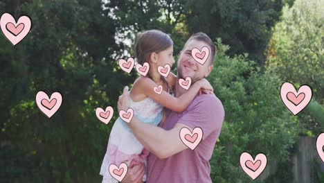 Animation-of-hearts-over-caucasian-father-hugging-his-daughter-in-garden