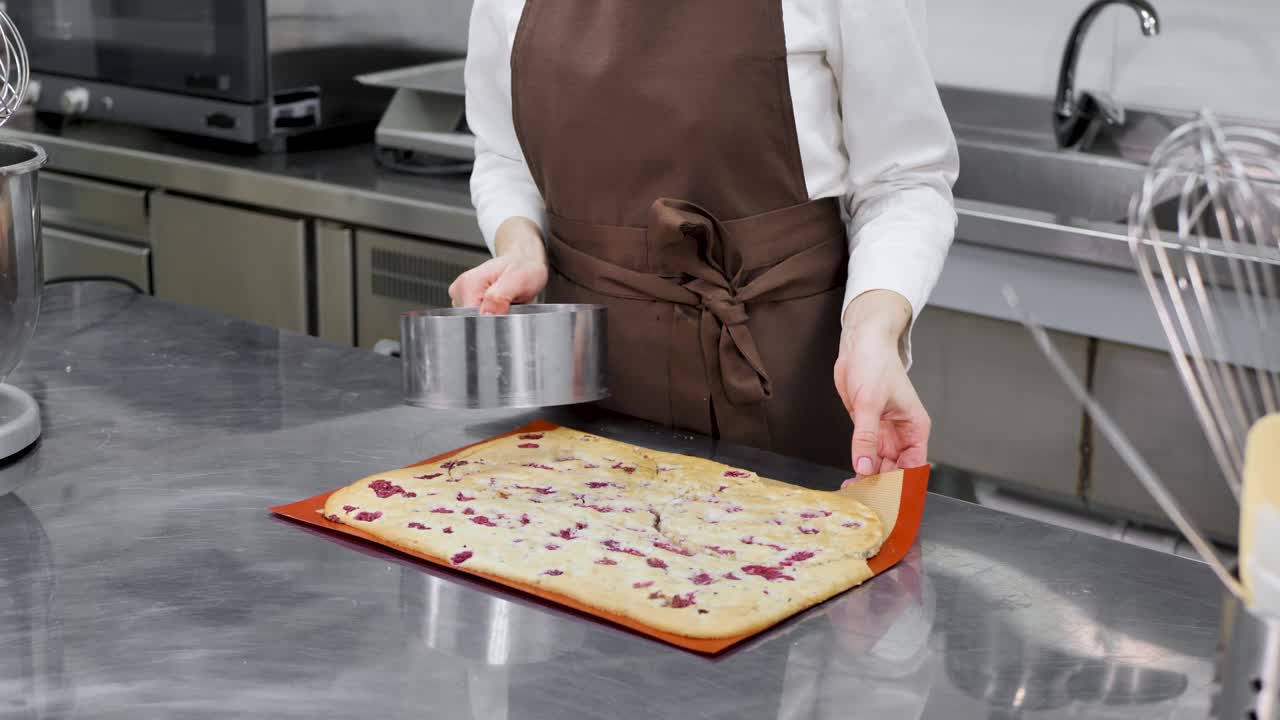 Female pastry chef cuts a round cake from a large biscuit dough in a professional kitchen