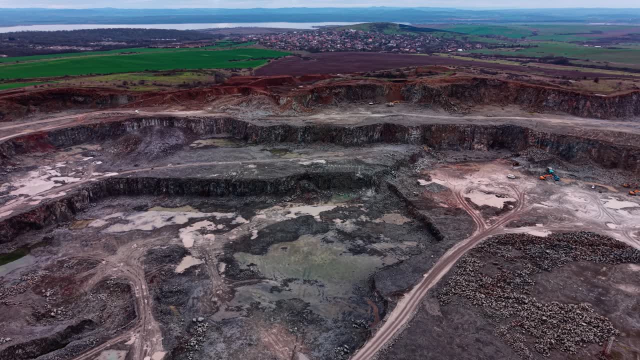 Granite quarry operation near a lake with green fields in the background