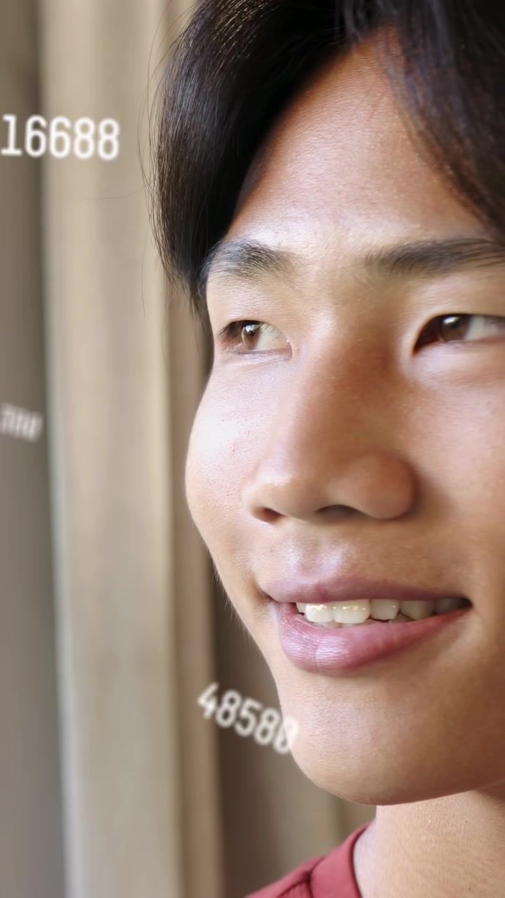 วิดีโอแนวตั้ง: เด็กวัยรุ่นชายที่หน้าต่าง เปลี่ยนสายตาและยิ้มพร้อมตัวเลขข้อมูลลอยอยู่บนใบหน้า