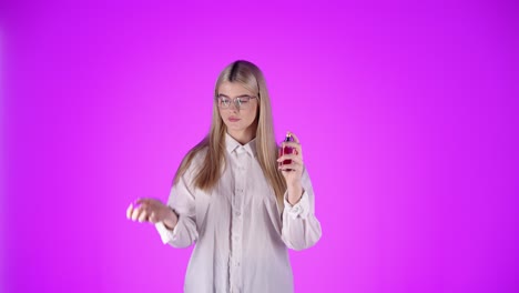 hermosa mujer joven rocia perfume en la muñeca para olerlo, fondo púrpura