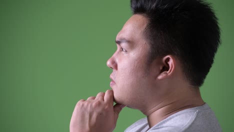 young handsome overweight asian man against green background