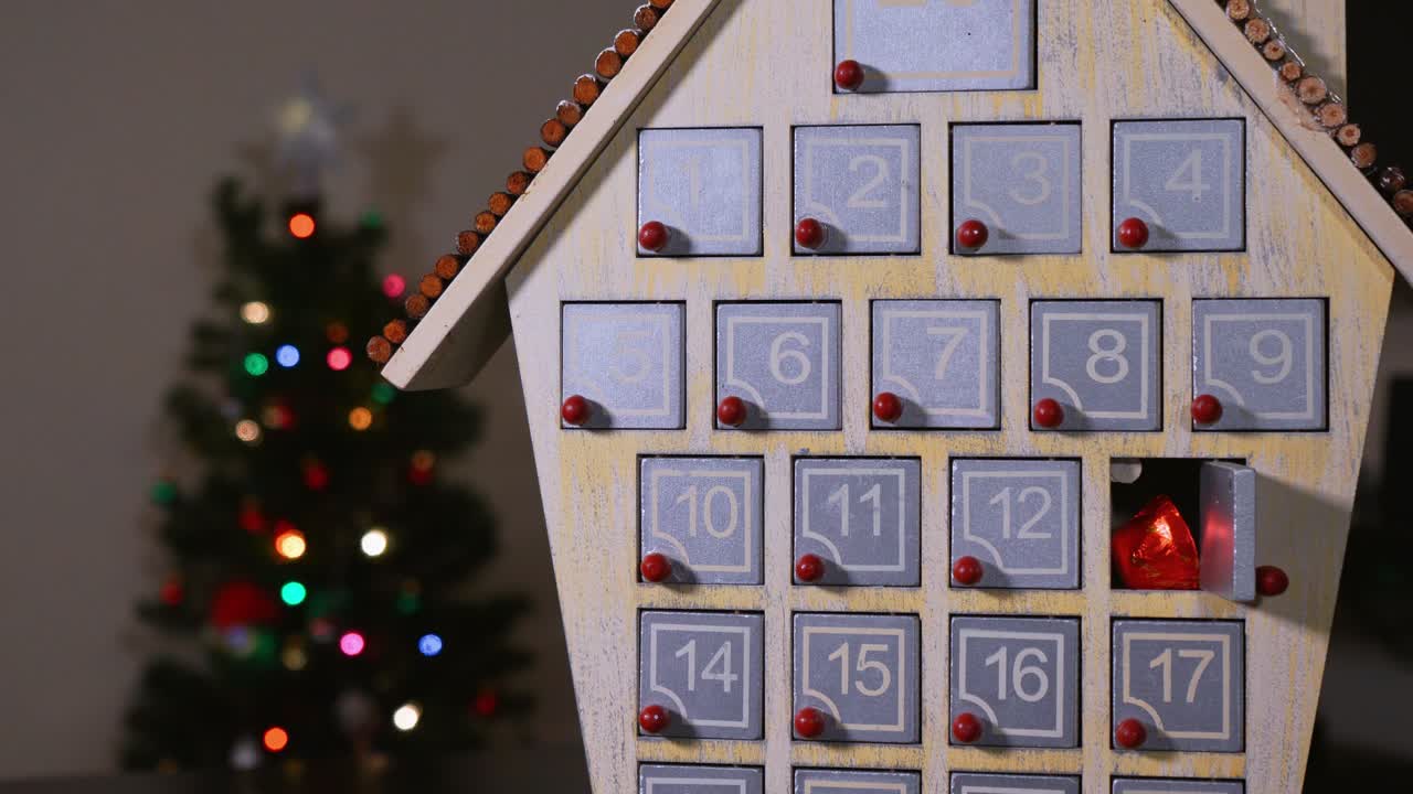 primer plano de una mano sacando dulces de un calendario de adviento de madera frente a un árbol de navidad