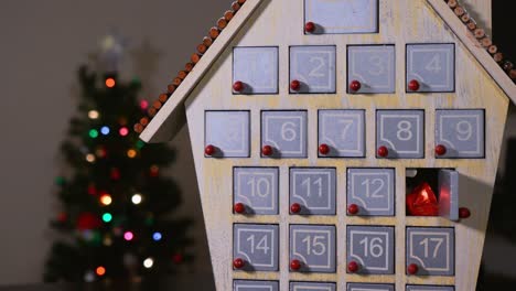 close up shot of a hand getting candy out of a wooden advent calender in front of a christmas tree