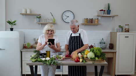 vegan senior grandparents looking for a culinary recipe online on digital tablet, cooking salad