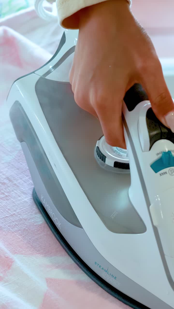 A person presses and glides a steam iron over a light-colored shirt on an ironing board in bright, natural daylight, focusing on removing wrinkles