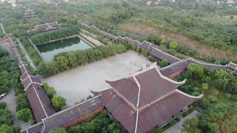 vista aérea de un avión no tripulado en vietnam volando sobre una zona de templo budista llena de árboles verdes frente a un río serpiente en ninh binh al atardecer