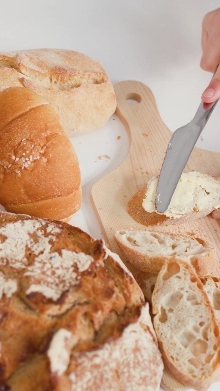 Close-up shot of hands spreading butter on sliced sourdough bread among various artisan pastries.