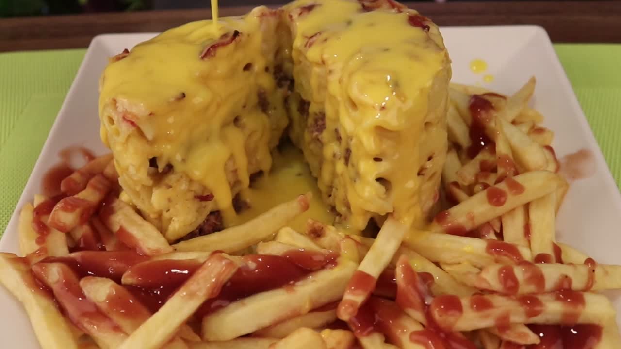 Přelévání sýrové omáčky přes burger s makarony se sýrem a hranolky