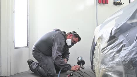 Man-wearing-protective-mask-spray-painting-vehicle-inside-modern-garage