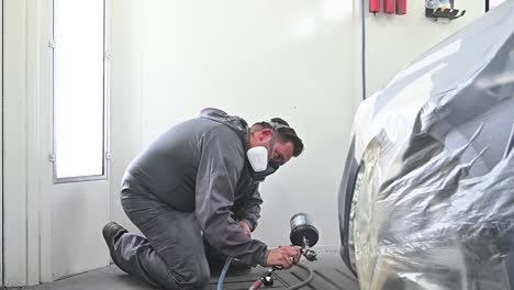 man wearing protective mask spray painting vehicle inside modern garage