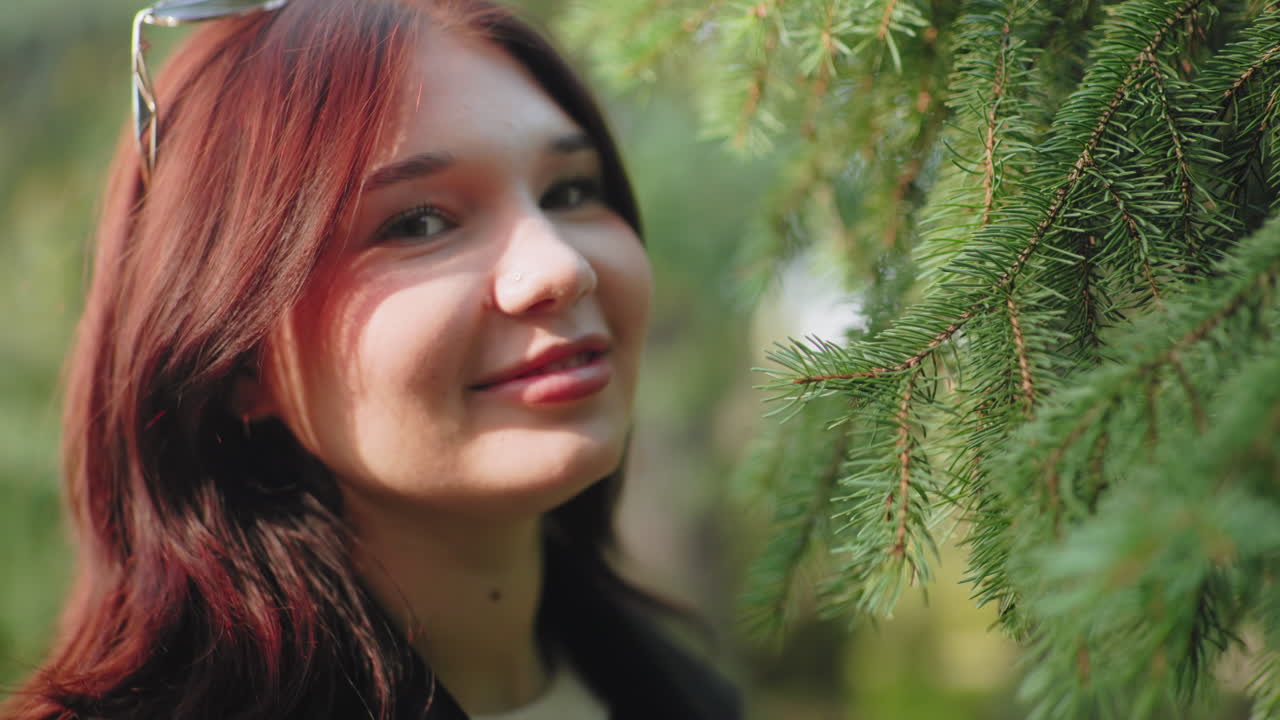 미소 짓는 표정으로 소나무 향기를 맡는 우아한 소녀의 클로즈업 인물 사진, 눈을 감은 채 숲 속에서 휴식을 취하는 모습, 부드러운 보케 배경, 자연광, 푸른 삼림 지대에서의 야외 휴식