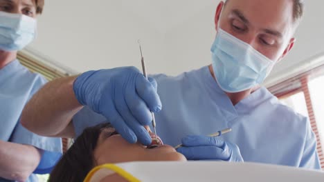 dentista maschio caucasico con maschera facciale che esamina i denti di una paziente femminile in una clinica dentale moderna