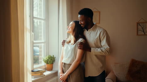 happy couple embracing and looking out window in sunlight