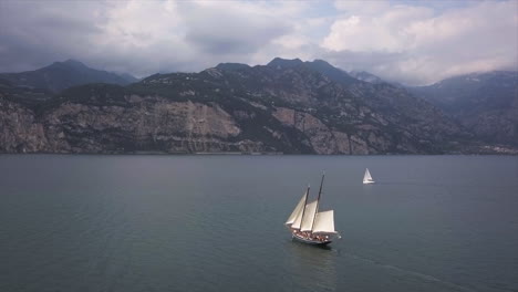 Velero-En-El-Lago-Di-Garda-Con-Acantilados-De-Garda-Al-Fondo-En-Un-Día-Parcialmente-Nublado