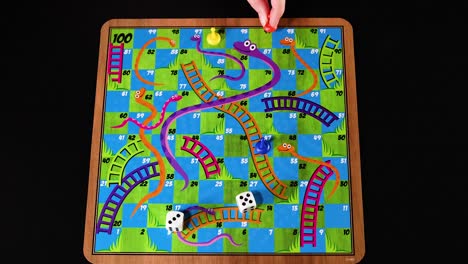 hands moving pieces on snakes and ladders board