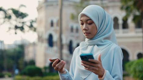 muslim woman in hijab using smartphone and credit card outdoors