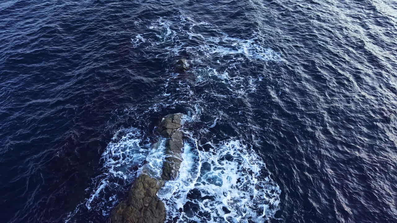 Onde oceaniche incantevoli danzano attorno a formazioni rocciose sotto il sole splendente a mezzogiorno, in un sereno paesaggio costiero
