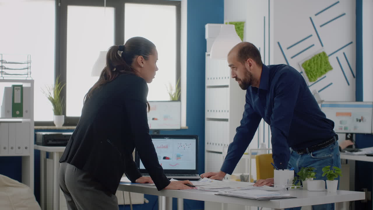 Man and woman using charts on laptop to plan strategy