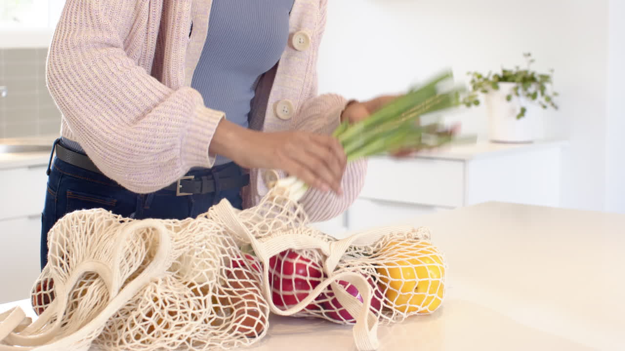 Woman in kitchen holding broccoli, unpacking groceries from reusable bag