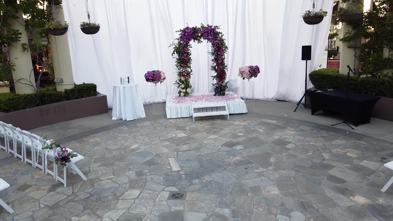 Vista ripresa dal drone in movimento all'indietro di un palco nuziale vuoto, cerimonia nuziale a cielo aperto e una fontana al centro della sala.