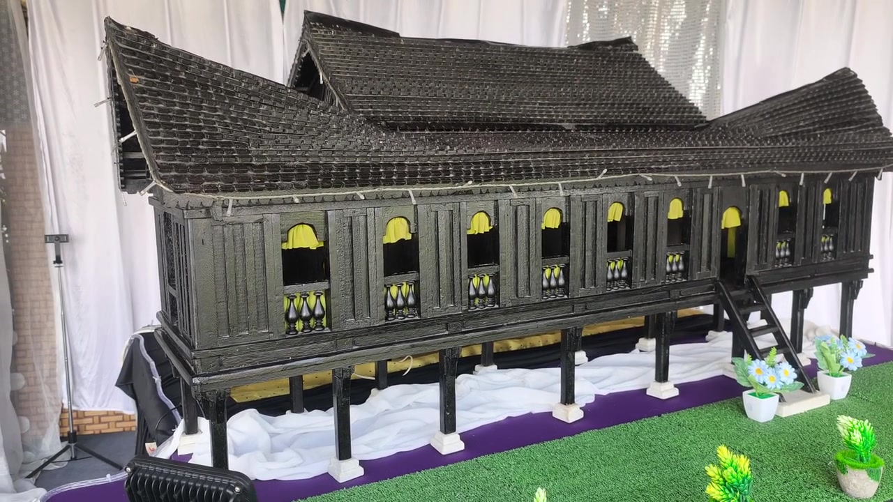 Một mô hình thu nhỏ của ngôi nhà truyền thống Negeri Sembilan Malay được trưng bày trên bàn. Du khách chiêm ngưỡng tác phẩm kiến trúc thủ công tinh xảo trong một cuộc triển lãm.