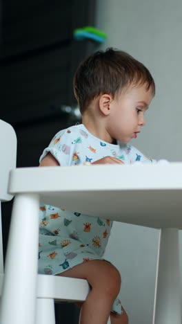 focused baby boy sits at white desk in his room. kid plays with his toys cheering and clapping hands. vertical video