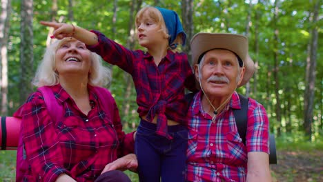 Old-senior-grandparents-couple-tourists-hikers-resting-in-forest-with-granddaughter-in-summer-wood