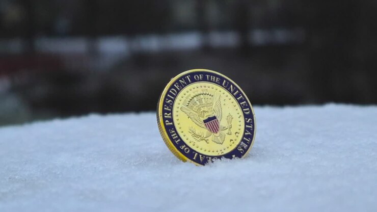 Gorgeous footage of United States golden Presidential Seal coin standing in white fluffy snow during winter time outdoors, while snow is falling on it and around it. Snow is melting on the coin.