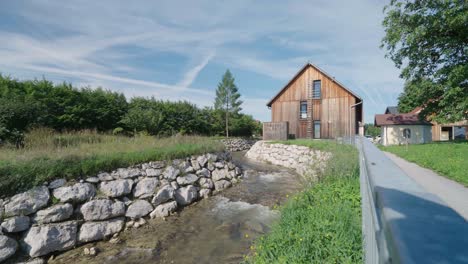 wide shot of a wooden house that has a river flowing on the left side