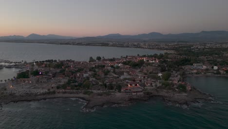 Vista-Aérea-Acercándose-Al-Casco-Antiguo-Barrio-Costero-Inmobiliario-Iluminado-Al-Atardecer