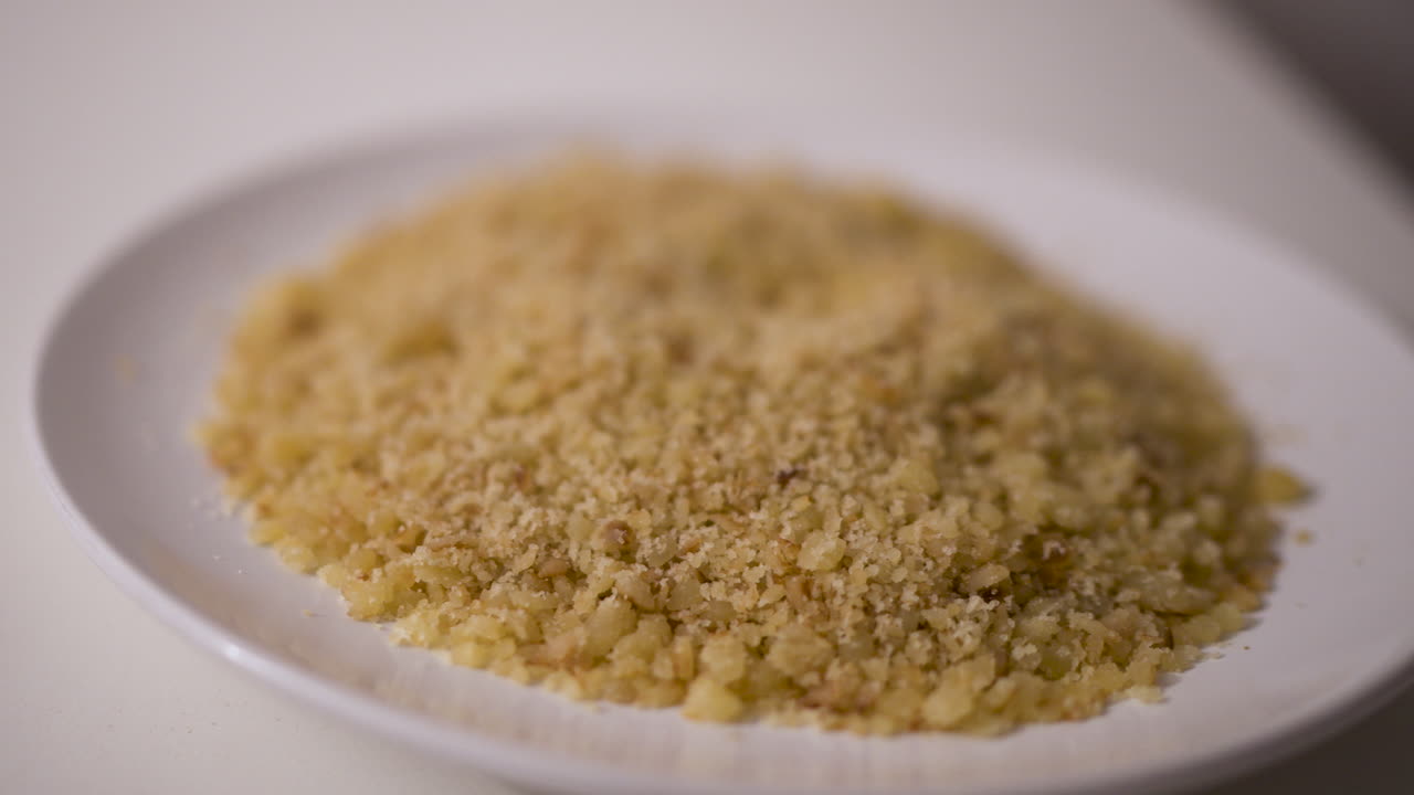Reviro, a rustic fried flour crumb dish typical of rural Argentina, is served dry on a white plate with its grainy texture highlighted in a smooth slow motion close-up angle.