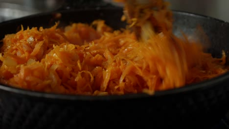 frying onions and grated carrots in a pan with oil. stir frying in skillet with wooden spatula