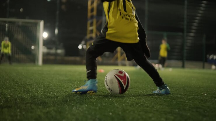 A children's football team trains at the stadium under the guidance of a coach. Kids in sports uniforms practice ball exercises, improve technique, and develop teamwork on the green field