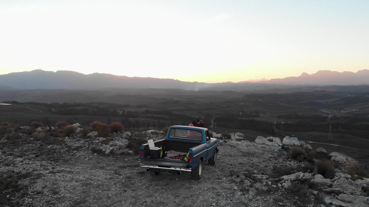 Coppia seduta sul portellone di un pickup che osserva una vista panoramica della valle, generando avvisi sui social media e mostrando metriche.