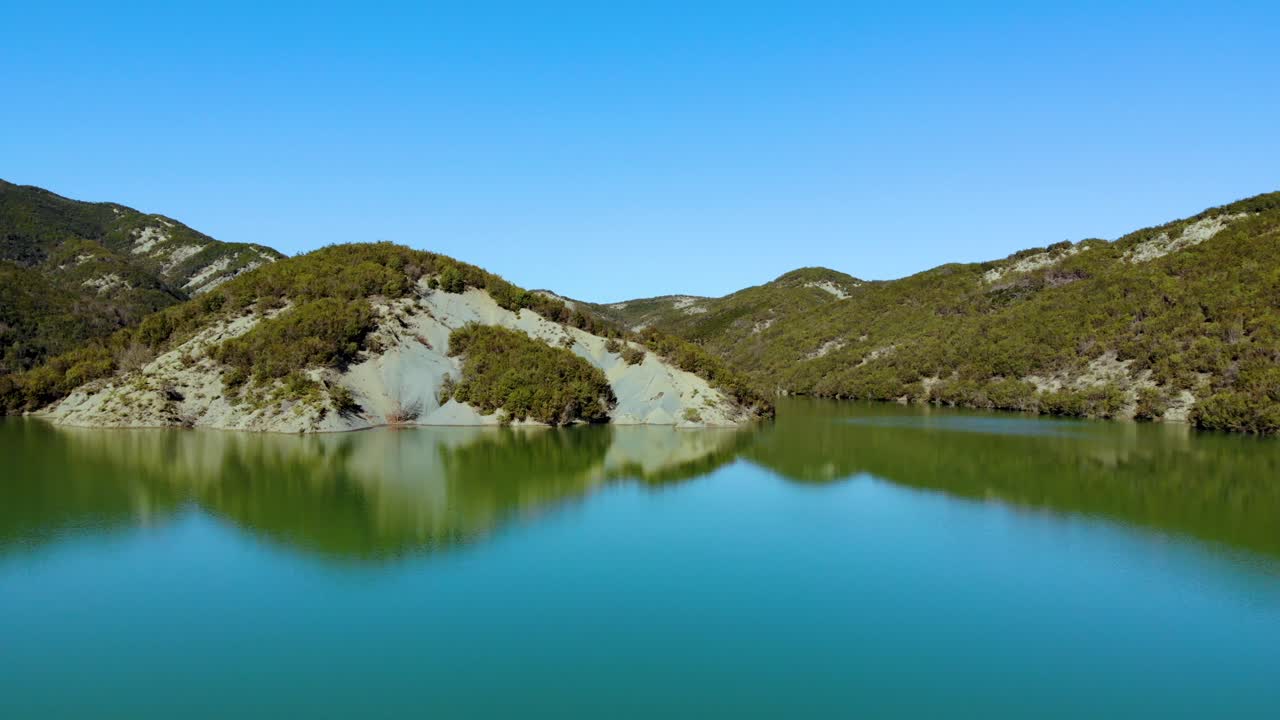 Fabulous lake with calm water surface reflecting beautiful mountains with green vegetation under bright blue sky