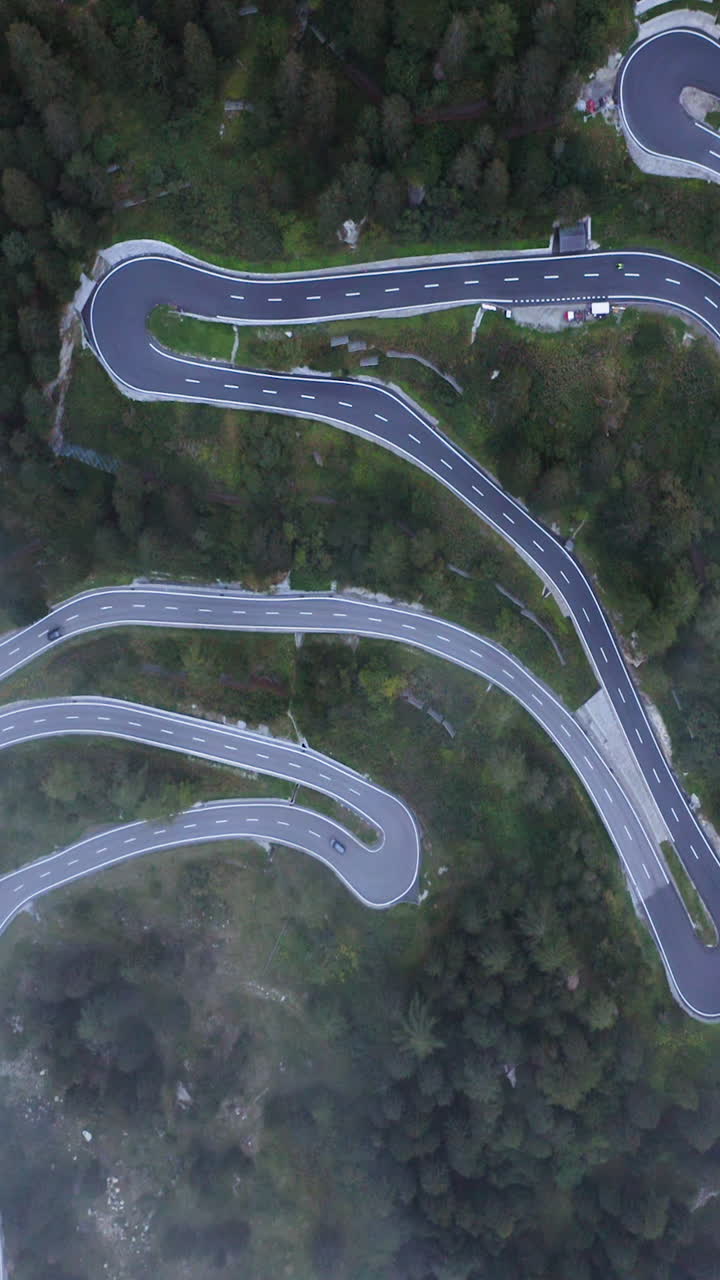 Vertical drone shot above traffic on a winding road, foggy day in the alps