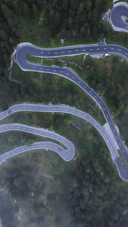 vertical drone shot above traffic on a winding road, foggy day in the alps