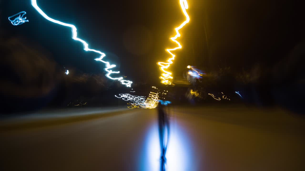 전기 스쿠터를 타고 빛나는 마을의 밤 거리를 가로질러 달리는 남자