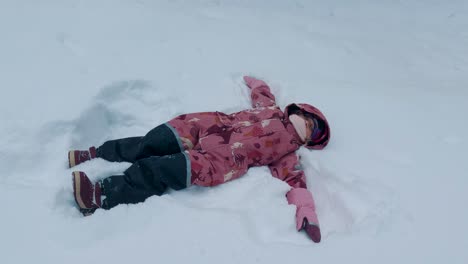 happy healthy baby girl makes a snow angel in the park on the in the deep snow