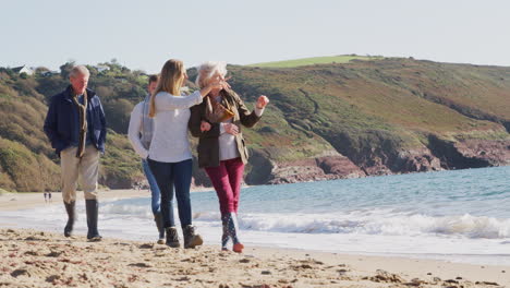 senior couple walking along shoreline with adult offspring on winter beach vacation