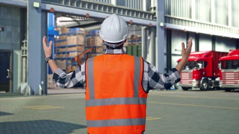 back view of a male engineer with safety helmet spreading arms while standing , outside of logistics distributions warehouse