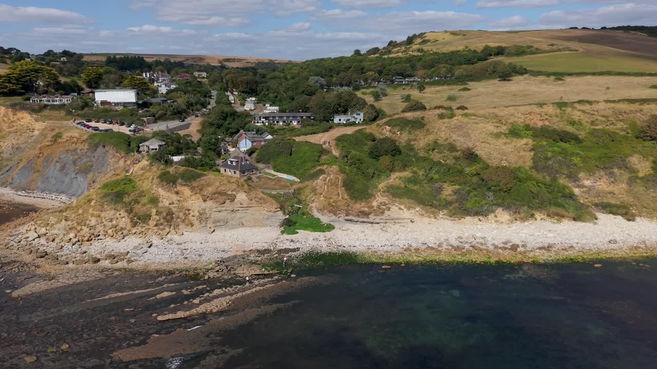 Stunning aerial drone footage of Osmington's dramatic Jurassic coastline in Dorset, England. Descending orbital shot reveals rugged landscape, rocky beach, rolling hills and coastal houses