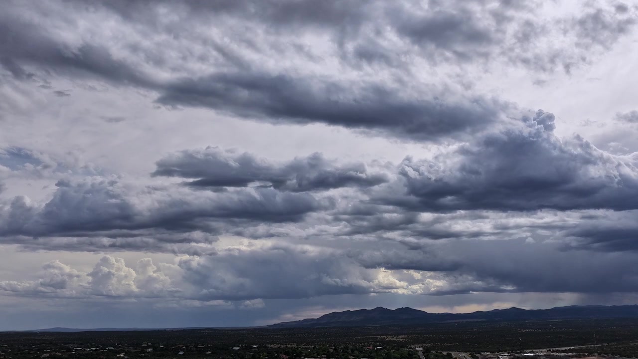 A moody drone timelapse capturing the dynamic formation of dark storm clouds. The heavy, overcast sky shifts and builds, highlighting active weather patterns and deep atmospheric instability.