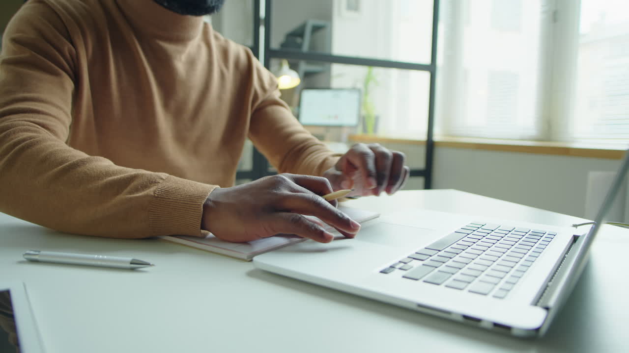 Black Man Working on Laptop and Taking Notes at Office Desk