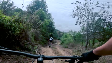 Dos-Ciclistas-Andan-En-Bicicleta-Por-Una-Carretera-Dentro-De-Un-Bosque,-Una-Colina-Y-Un-Pueblo-En-Guatemala,-América-Del-Norte